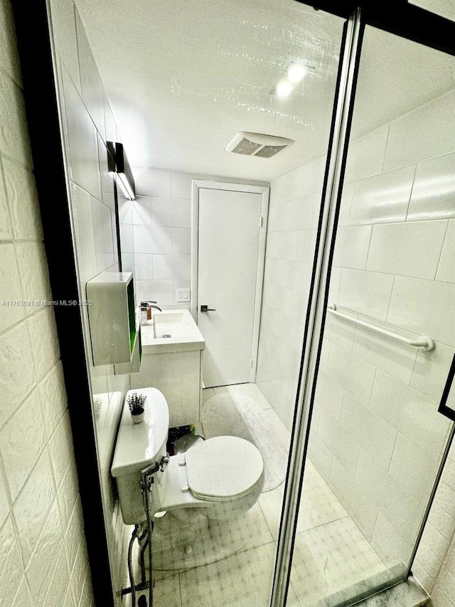 bathroom with tile walls, toilet, visible vents, and a stall shower