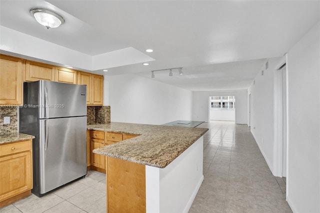 kitchen with light stone counters, light tile patterned floors, a peninsula, freestanding refrigerator, and decorative backsplash