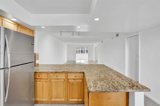 kitchen with visible vents, freestanding refrigerator, a peninsula, rail lighting, and light stone countertops