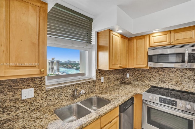 kitchen with light brown cabinetry, a sink, backsplash, appliances with stainless steel finishes, and light stone countertops