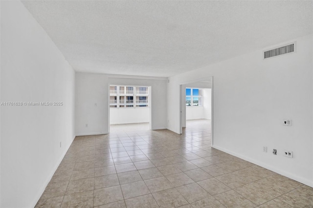 empty room featuring light tile patterned flooring, visible vents, a textured ceiling, and baseboards