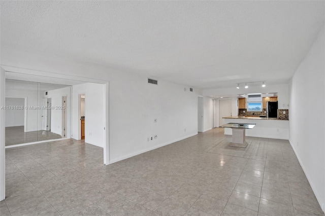 unfurnished living room featuring baseboards, visible vents, and a textured ceiling