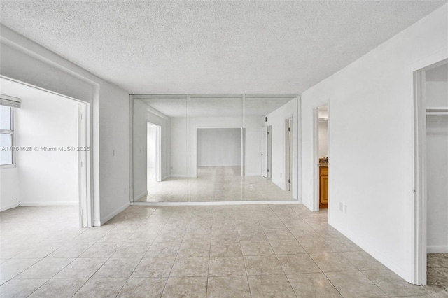 spare room with light tile patterned floors, baseboards, and a textured ceiling