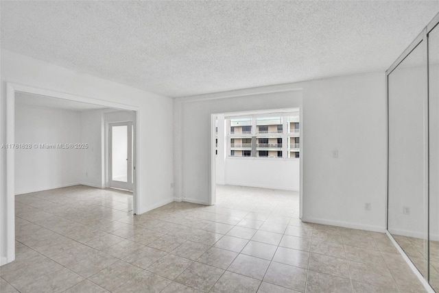 unfurnished room featuring light tile patterned floors, baseboards, and a textured ceiling