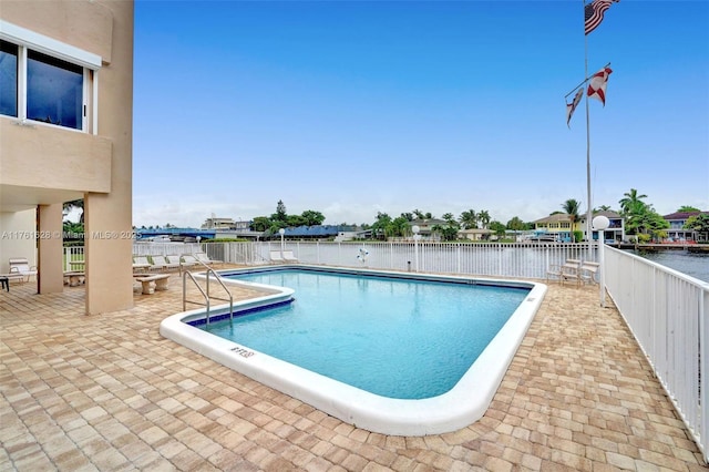 pool with a patio, a water view, and fence