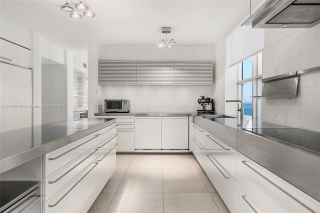 kitchen with light tile patterned floors, a sink, stainless steel countertops, white cabinets, and stainless steel microwave