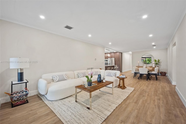 living room with visible vents, recessed lighting, crown molding, light wood finished floors, and baseboards