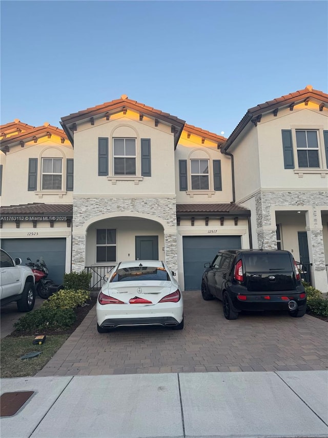 view of front of home with a garage, a tiled roof, decorative driveway, and stone siding