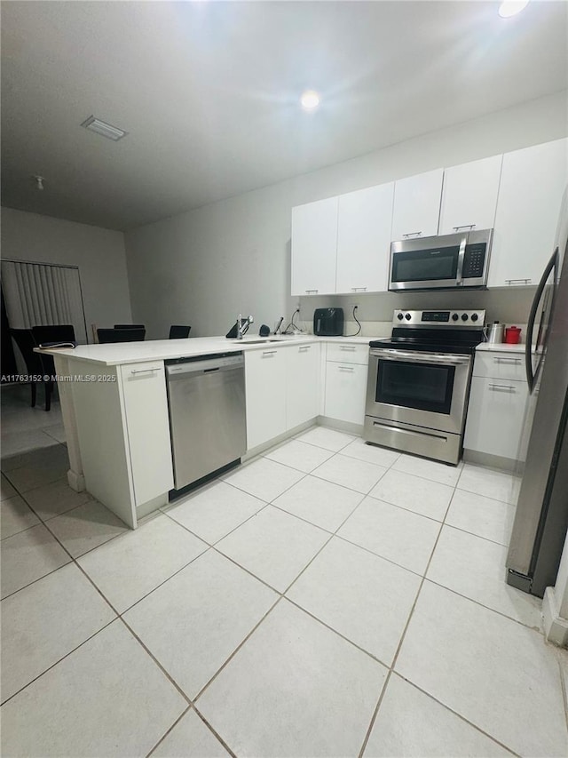 kitchen with light countertops, light tile patterned floors, appliances with stainless steel finishes, a peninsula, and white cabinetry