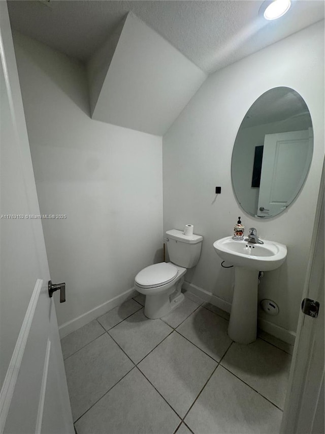 bathroom featuring tile patterned floors, toilet, a textured ceiling, baseboards, and vaulted ceiling