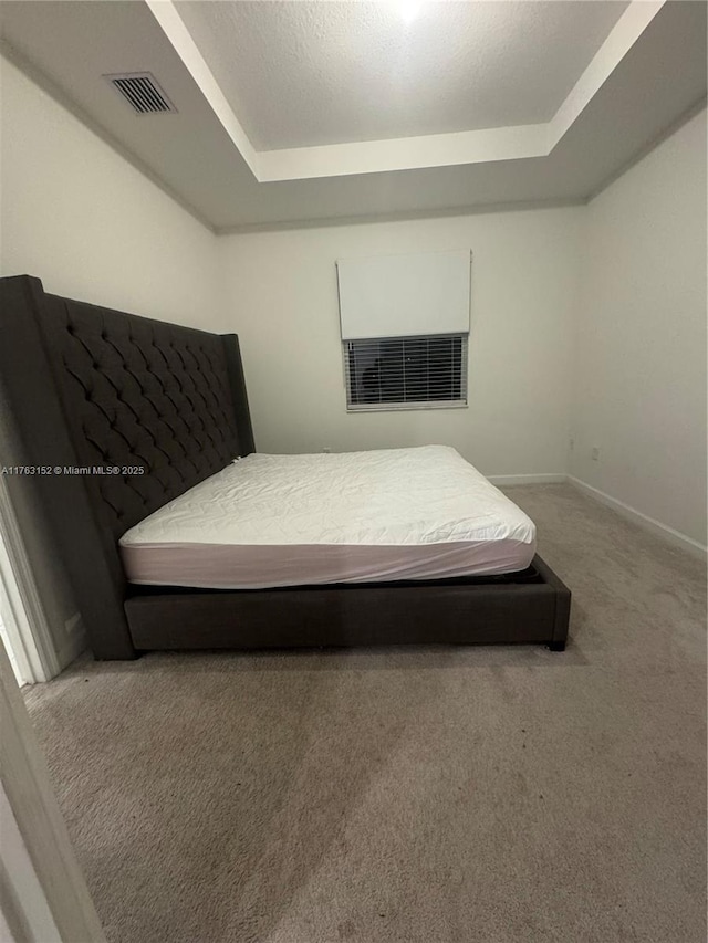 carpeted bedroom with a raised ceiling, baseboards, and visible vents