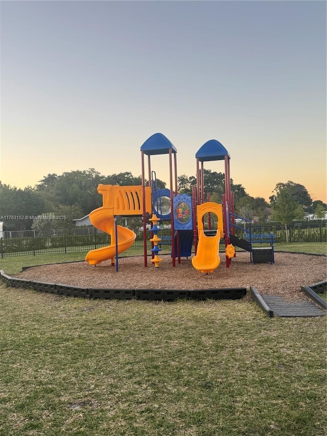 playground at dusk featuring playground community, a yard, and fence