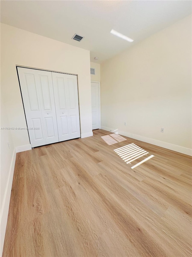 unfurnished bedroom featuring visible vents, light wood-type flooring, a closet, and baseboards