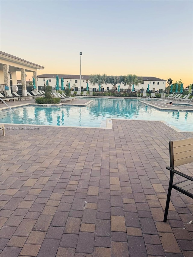 pool at dusk with a patio area and a community pool