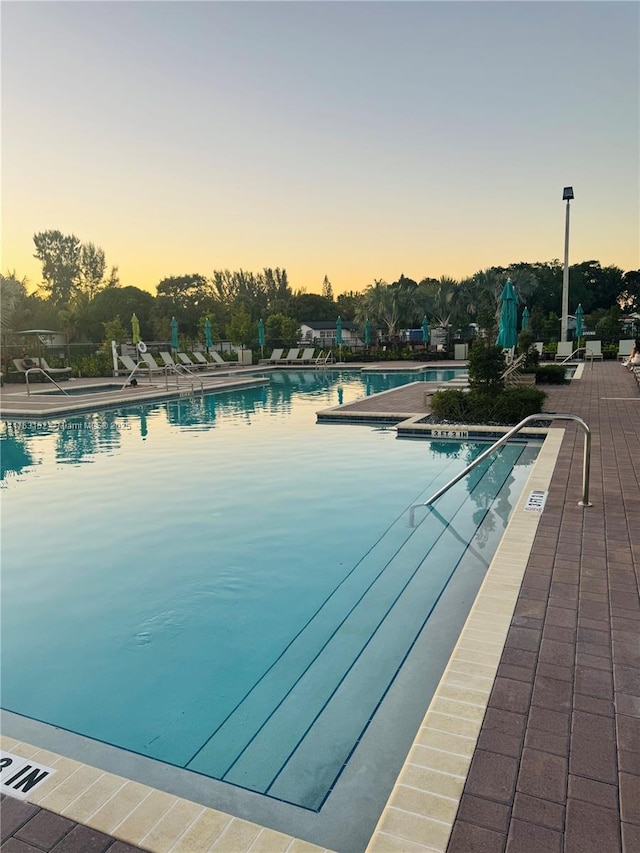 pool at dusk featuring a community pool and a patio