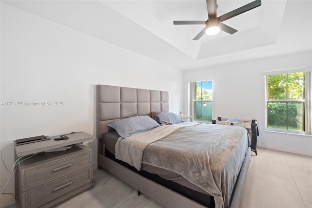 bedroom featuring light tile patterned floors, baseboards, a raised ceiling, and ceiling fan