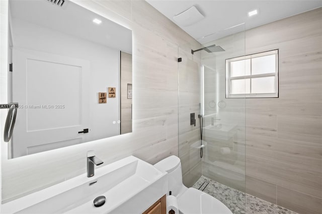 bathroom featuring vanity, visible vents, walk in shower, tile walls, and toilet