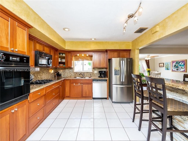 kitchen featuring visible vents, backsplash, brown cabinets, black appliances, and a sink