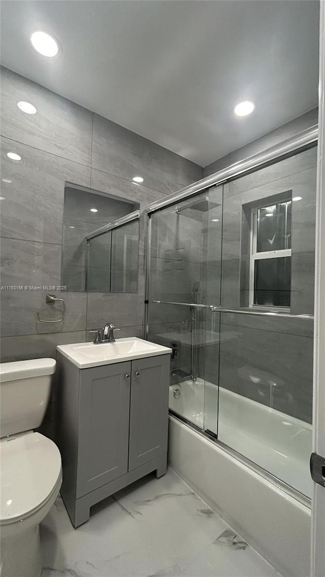 bathroom featuring vanity, enclosed tub / shower combo, tile walls, toilet, and marble finish floor