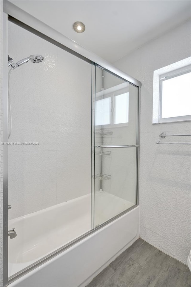 full bath with toilet, wood finished floors, bath / shower combo with glass door, and a healthy amount of sunlight