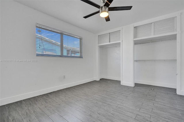 unfurnished bedroom with wood finished floors, baseboards, two closets, and ceiling fan