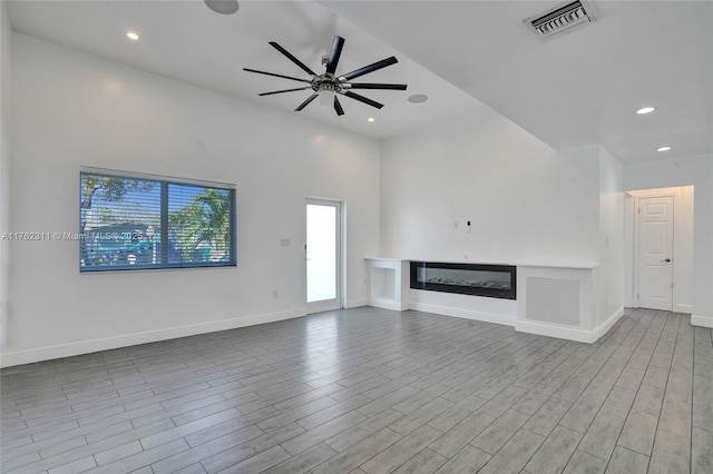 unfurnished living room featuring ceiling fan, visible vents, wood finished floors, and a glass covered fireplace