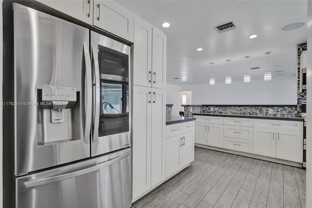 kitchen with visible vents, dark countertops, stainless steel fridge, white cabinets, and decorative backsplash