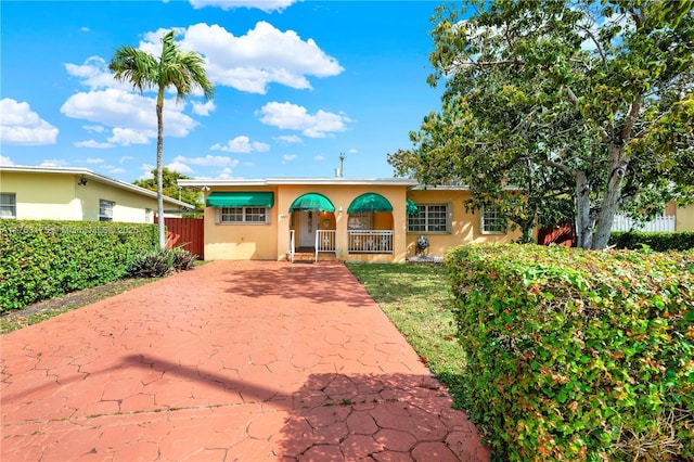 single story home with stucco siding, a porch, a front yard, and fence