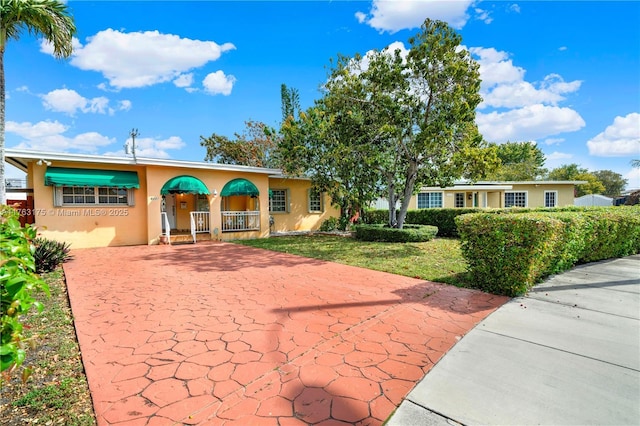 single story home featuring stucco siding, driveway, a porch, and a front yard