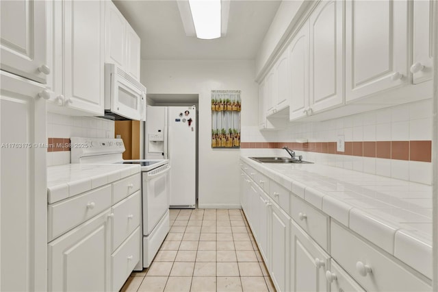 kitchen featuring white appliances, white cabinets, tile counters, and a sink