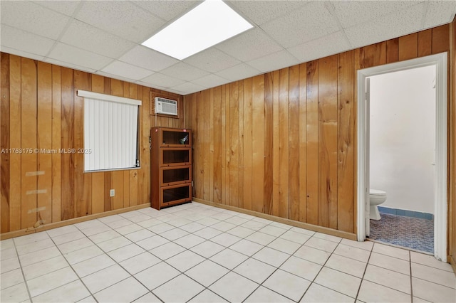 unfurnished room featuring a drop ceiling, baseboards, wooden walls, and an AC wall unit