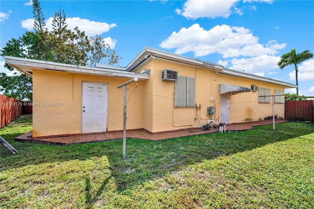 back of house featuring stucco siding, a lawn, a wall mounted AC, and fence