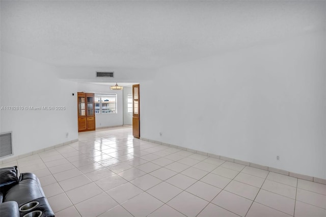 empty room featuring light tile patterned flooring, visible vents, a textured ceiling, and baseboards