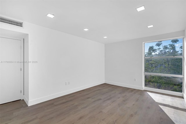 empty room featuring wood finished floors, visible vents, and baseboards