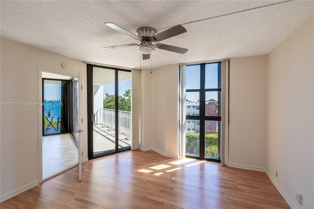 empty room featuring a textured ceiling, wood finished floors, floor to ceiling windows, baseboards, and ceiling fan