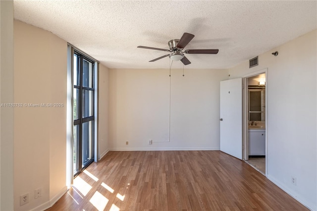 empty room with visible vents, a textured ceiling, wood finished floors, floor to ceiling windows, and ceiling fan