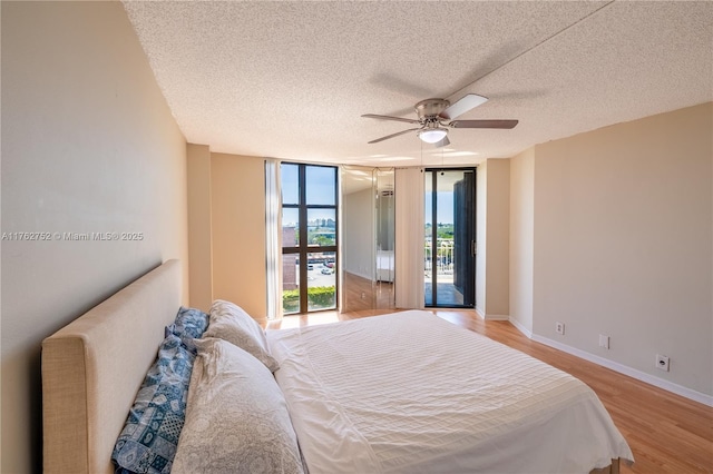 bedroom with light wood-style flooring, a ceiling fan, expansive windows, baseboards, and access to exterior