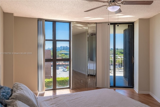 unfurnished bedroom with a textured ceiling, wood finished floors, floor to ceiling windows, baseboards, and access to exterior