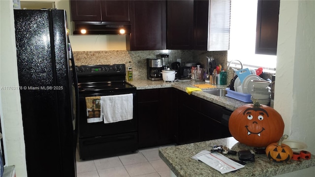 kitchen featuring under cabinet range hood, light stone countertops, black appliances, and a sink