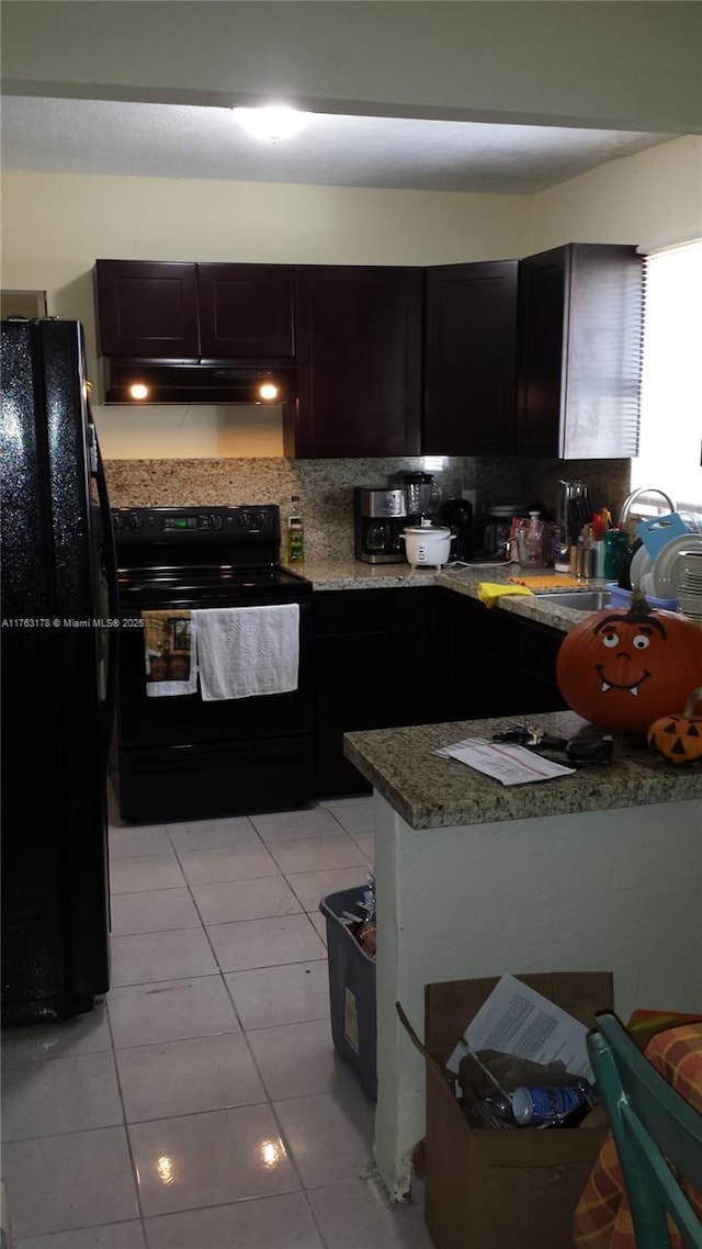 kitchen with under cabinet range hood, light tile patterned floors, decorative backsplash, black appliances, and a sink