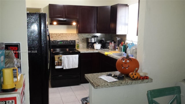 kitchen featuring under cabinet range hood, dark brown cabinetry, light tile patterned floors, black appliances, and a sink