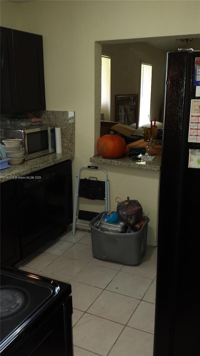 kitchen with light tile patterned floors, stainless steel microwave, light countertops, and black range with electric stovetop