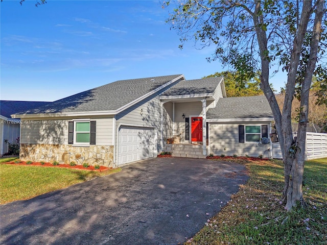 single story home featuring an attached garage, a shingled roof, a front yard, stone siding, and driveway