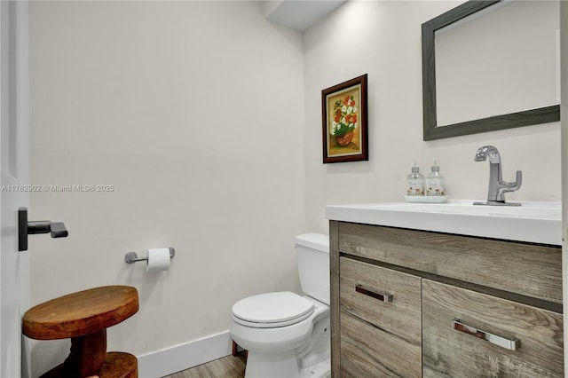 half bathroom featuring toilet, vanity, baseboards, and wood finished floors