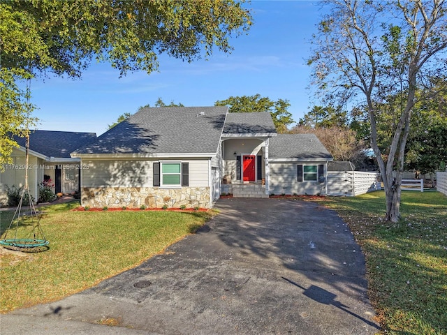 ranch-style home featuring fence, aphalt driveway, a front yard, roof with shingles, and stone siding