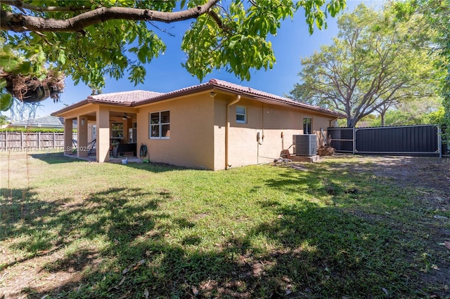 rear view of house with fence, a yard, central AC, ceiling fan, and stucco siding