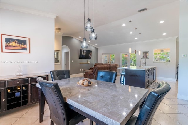 dining room featuring baseboards, ornamental molding, vaulted ceiling, light tile patterned flooring, and arched walkways