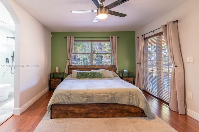 bedroom with access to exterior, baseboards, wood finished floors, arched walkways, and a ceiling fan