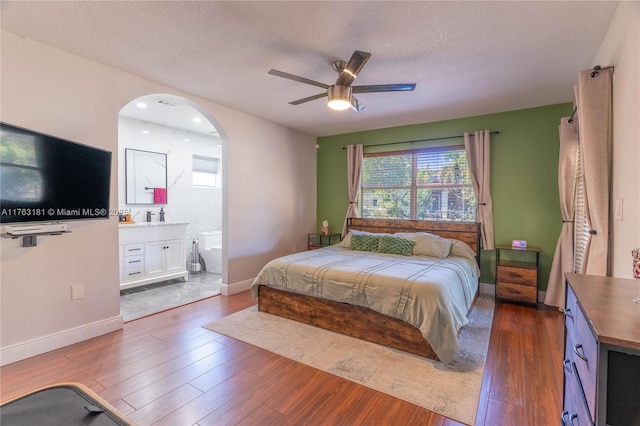 bedroom with a textured ceiling, ensuite bathroom, baseboards, and wood finished floors