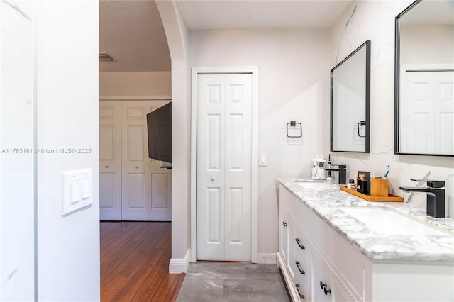 bathroom featuring wood finished floors, double vanity, a sink, decorative backsplash, and a closet